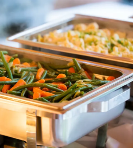 Tray of cooked green beans and carrots, with another tray of cauliflower in the background.